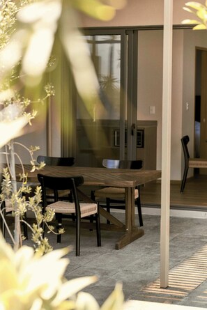 A modern dining area with a wooden table and chairs, a glass partition, and a view of the interior.