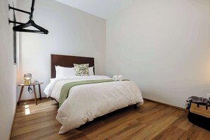 A hotel room with a bed, a bedside table with a lamp, and a hanging coat rack.