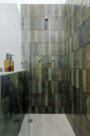 A shower area with a glass door, a white shelf with a bottle, and a drain.