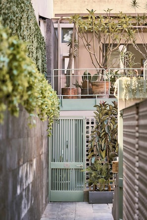 A narrow alleyway with a green gate, potted plants, and a building with a balcony.