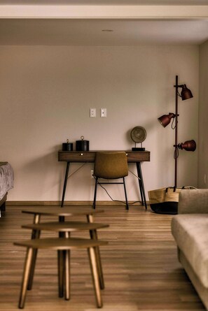 A room with a wooden floor, a desk with a chair, a lamp, and a bed.
