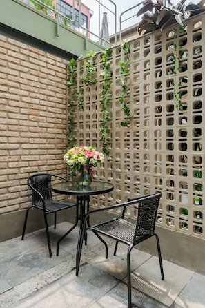 A patio area with a brick wall, a green trellis with climbing plants, and two black metal chairs around a glass table with a vase of flowers. - Zaterra: A Tranquil Oasis in Roma Norte. (Ciudad de México)