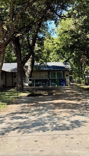 A residential area with a house, large trees, and a paved driveway.