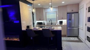 Una cocina moderna con una isla central, taburetes de bar, microondas integrado y un refrigerador de acero inoxidable.