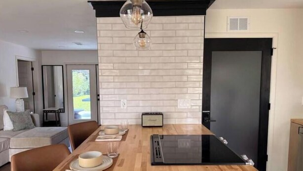 Una cocina moderna con una mesa de madera dispuesta para comer, un refrigerador negro y un revestimiento de ladrillo blanco.