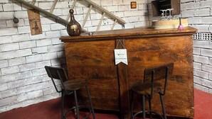Un rincón de bar rústico con una barra de madera, dos taburetes, una botella antigua y un letrero que indica barra de agua y champán.