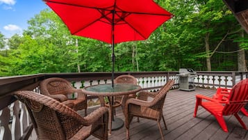 Relax on our spacious wraparound deck featuring comfortable outdoor lounge furniture, Adirondack chairs, and shaded seating beneath a red umbrella. Enjoy morning coffee, fresh mountain air, and peaceful forest views at The Crimson Cocoa Chalet.