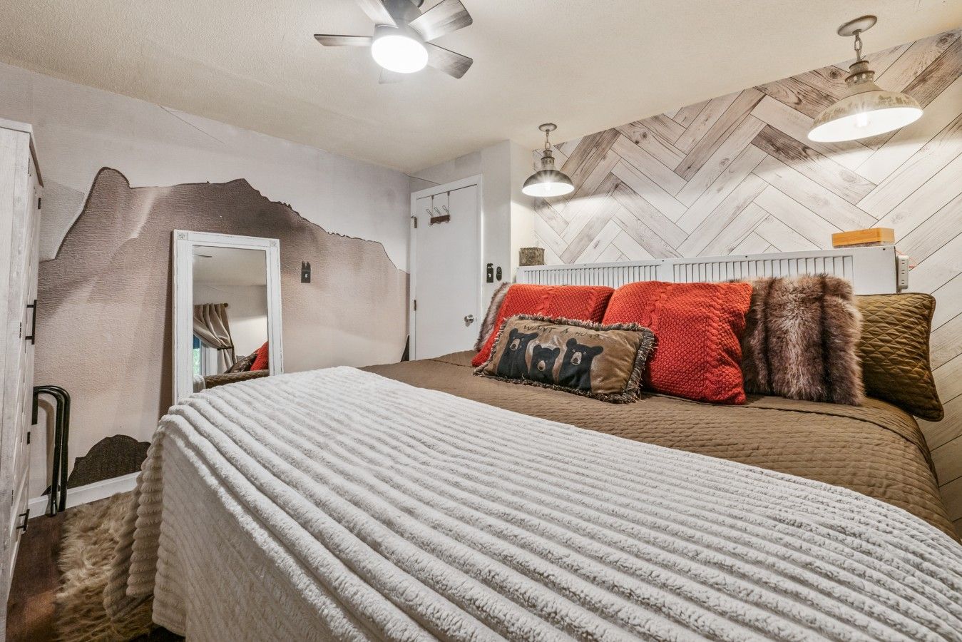 A bedroom with a bed, a mirror, a door, and a herringbone-patterned wall.