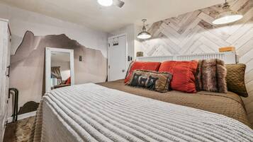 A bedroom with a bed, a mirror, a door, and a herringbone-patterned wall.
