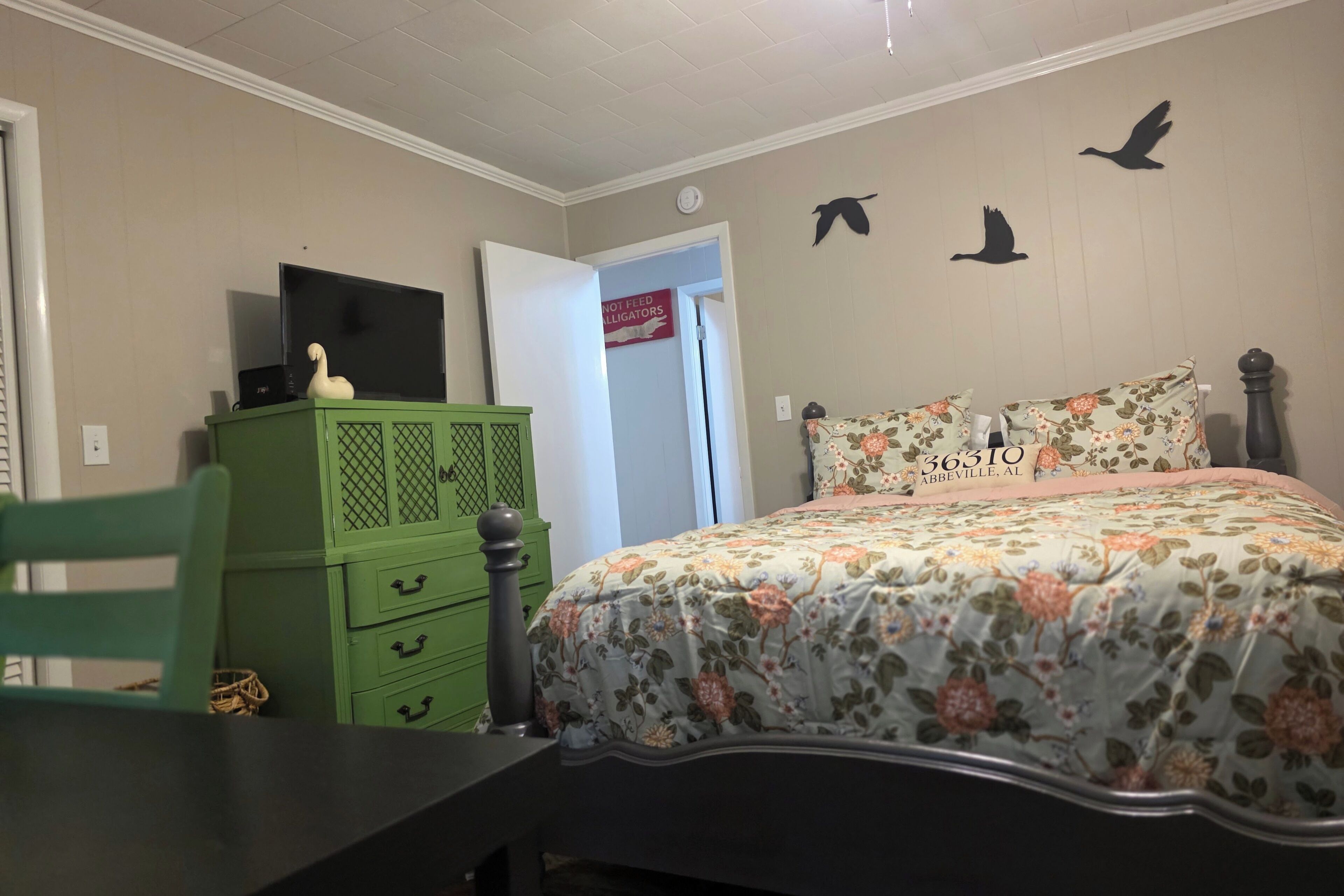 Un dormitorio con cama, cómoda verde y televisor encima.