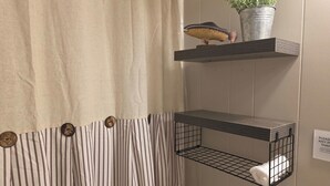 Une salle de bain avec des rideaux à rayures, un porte-serviettes avec une serviette, et une étagère avec une plante et une figurine de poisson.