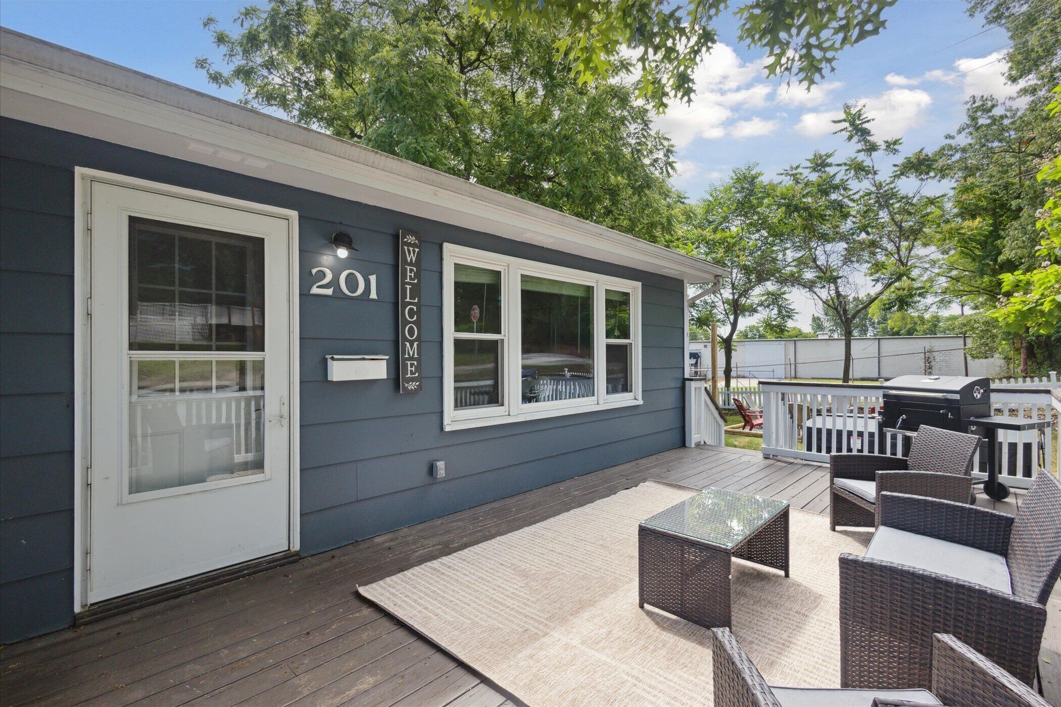 A house with a 'WELCOME' sign, number 201, and a deck with outdoor furniture.