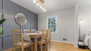 A dining area with a wooden table and chairs, a round mirror, and a window with a view of greenery. - Cozy Home w/ Pool Table, Arcade & Firepit (Spartanburg)