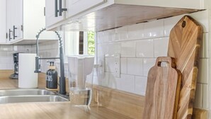 A modern kitchen with white cabinets, a wooden countertop, and a built-in cutting board. - Cozy Home w/ Pool Table, Arcade & Firepit (Spartanburg)