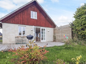A red barn with a patio, a grill, and a wooden fence. - 5 Person Holiday Home in Lundby (Lundby)