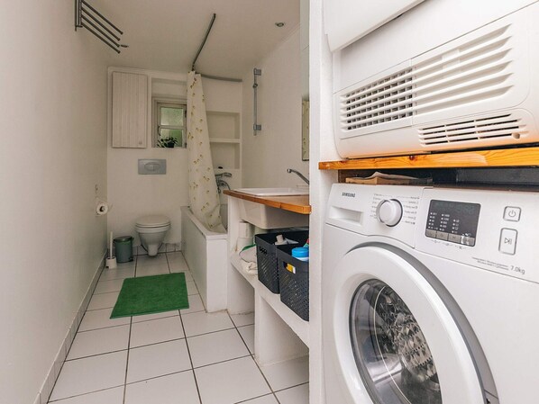 Une petite buanderie comprenant un lave-linge, un petit évier et des toilettes.