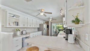 Una cocina moderna con armarios blancos, una isla central y un ventilador de techo.