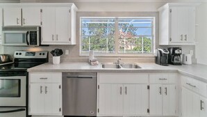 Una cocina moderna con armarios blancos, lavavajillas de acero inoxidable, pileta doble y microondas.