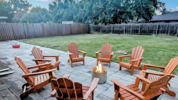 Un patio con sillas Adirondack dispuestas alrededor de un hogar para fuego central.
