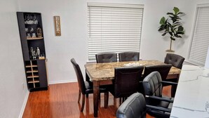 Un comedor con una mesa de madera, sillas de cuero negro, un armario negro con cristalería y un cartel con la palabra 'BEER'.