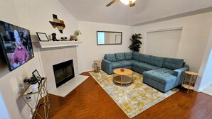 Una sala de estar con chimenea, un sofá modular, una mesa de centro redonda y un ventilador de techo.