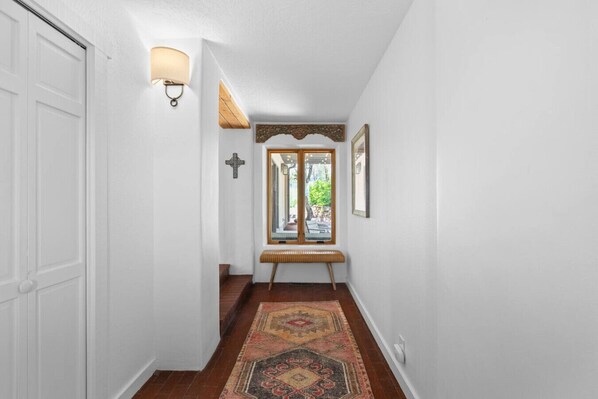 A hallway with a white door, a wall-mounted light fixture, a bench, and a patterned rug.