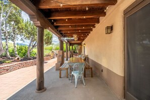 Un patio al aire libre con una pérgola de madera, una mesa con sillas y un muro de ladrillo.