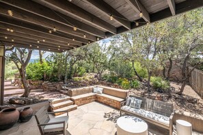 Un patio exterior cubierto con suelo de piedra, un banco integrado y una zona de estar con cojines.