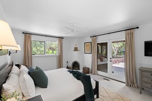 Ein Schlafzimmer mit Bett, Kamin, Fernseher und einer Schiebetür zu einem Außenbereich.