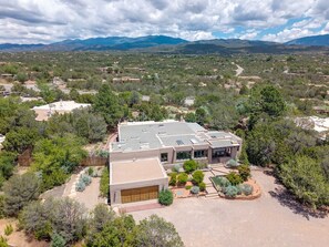 A modern house with a large garage, surrounded by a landscaped garden and a view of distant mountains.