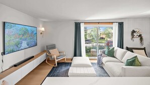 Een moderne woonkamer met een bank, een schommelstoel, een flatscreen televisie en uitzicht op buiten.
