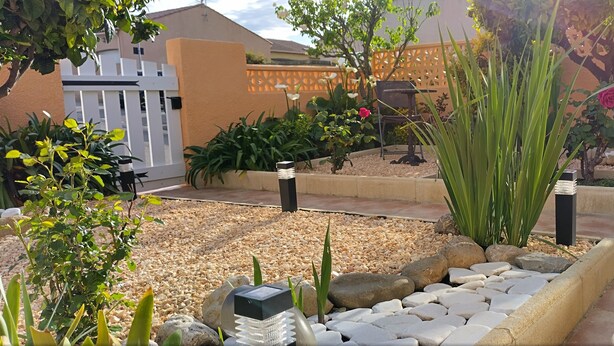 Ein Garten mit Pflanzen, einem weißen Zaun und einer gepflasterten Fläche.