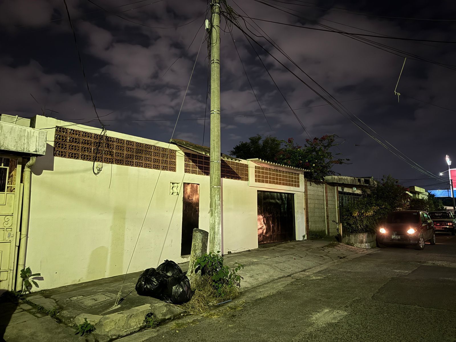 A nighttime street scene with a building, a parked car, and a utility pole.