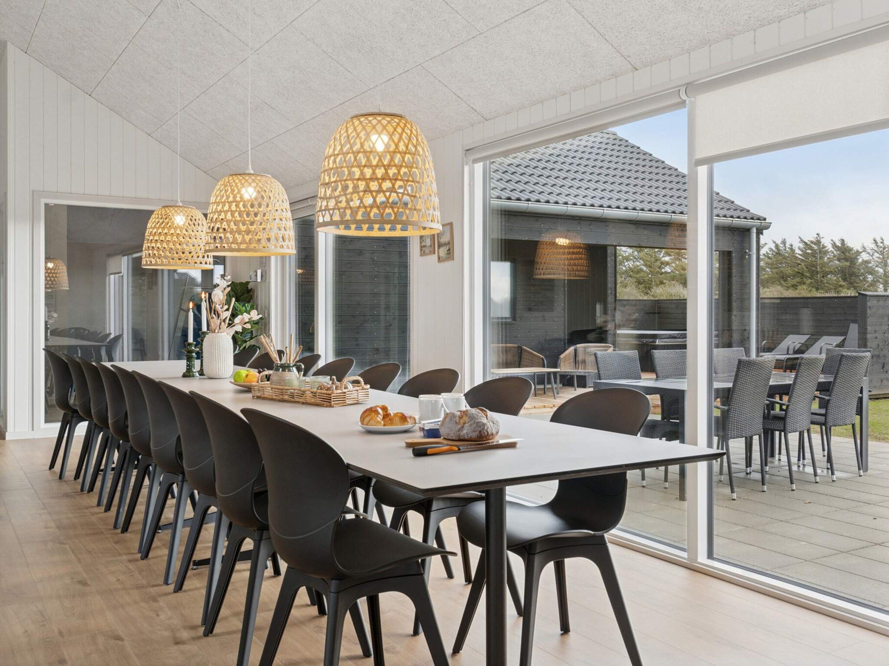 Een moderne eetruimte met een lange tafel, zwarte stoelen en hangende lampen.