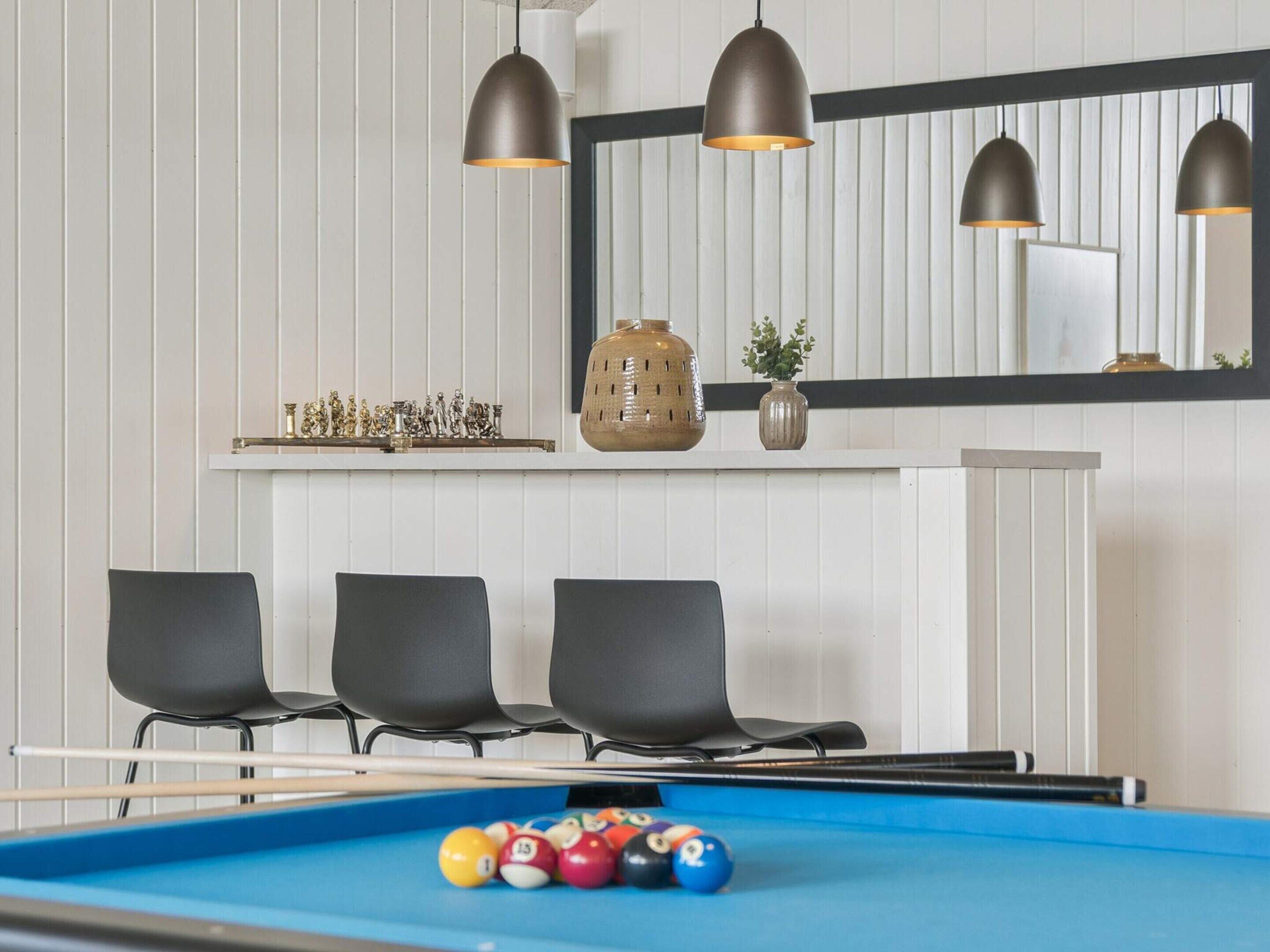 A pool table with balls, three black chairs, and pendant lights.
