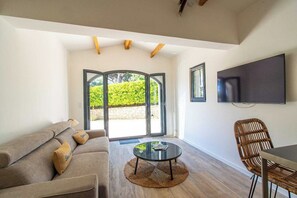 A living room with a sofa, a round coffee table, a wicker chair, a flat-screen TV, and a glass door leading outside.
