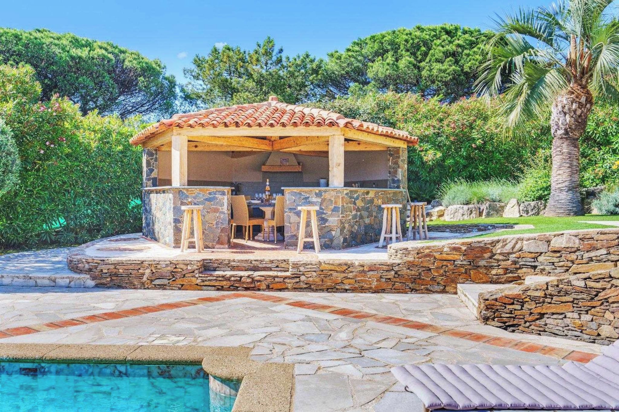 Un espace bar extérieur abrité, doté de murs en pierre et d’une piscine.