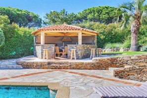 A covered outdoor bar area with stone walls and a pool.