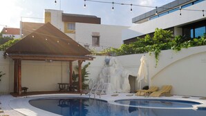 Una piscina con un pabellón de madera, sillas de descanso y una pequeña cascada.