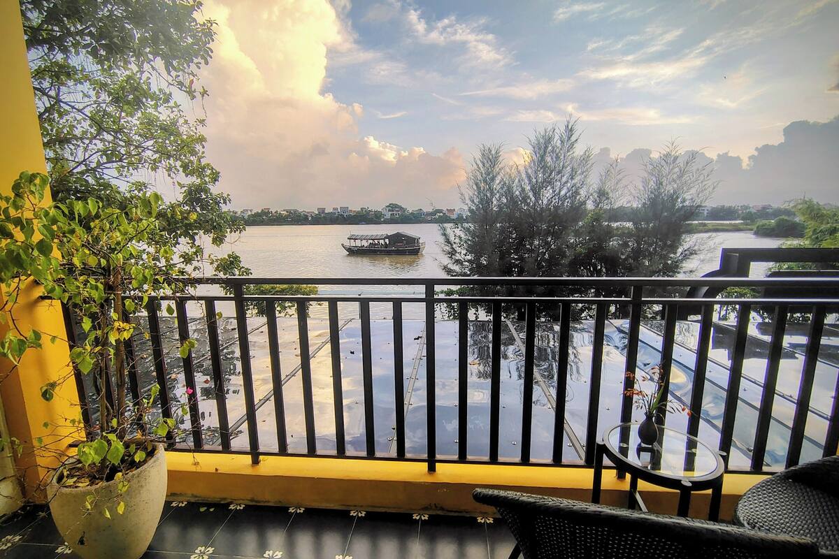 A balcony with a view of a river, a boat, and a potted plant.