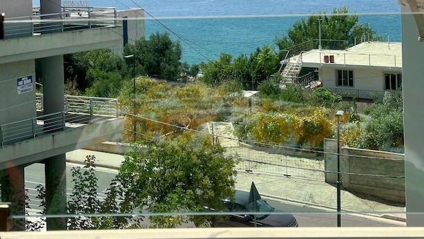 A view from a balcony overlooking a coastal area with buildings, a road, and a clear sky.