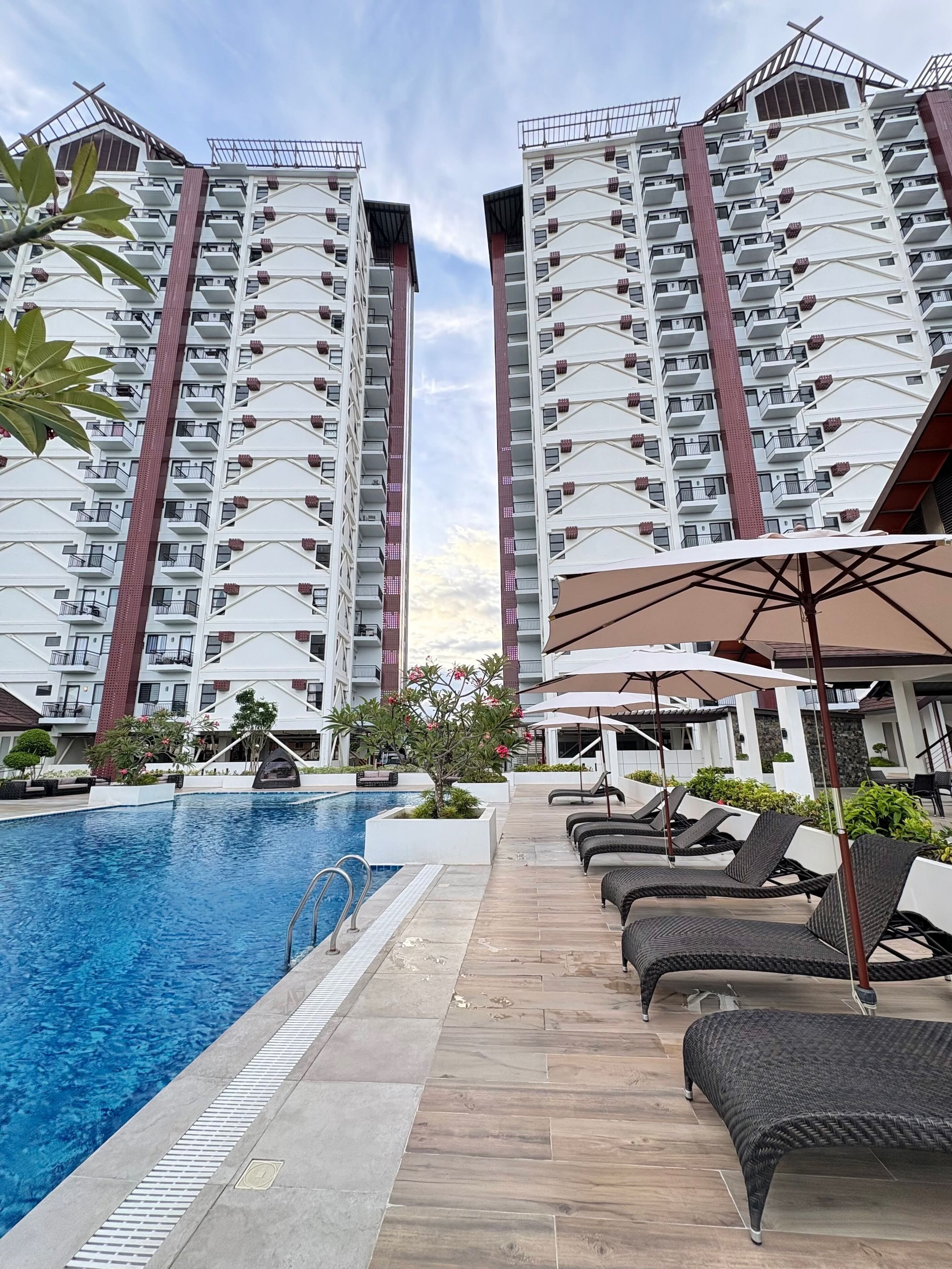 Una piscina con sillas de descanso y sombrillas, rodeada de edificios residenciales altos.