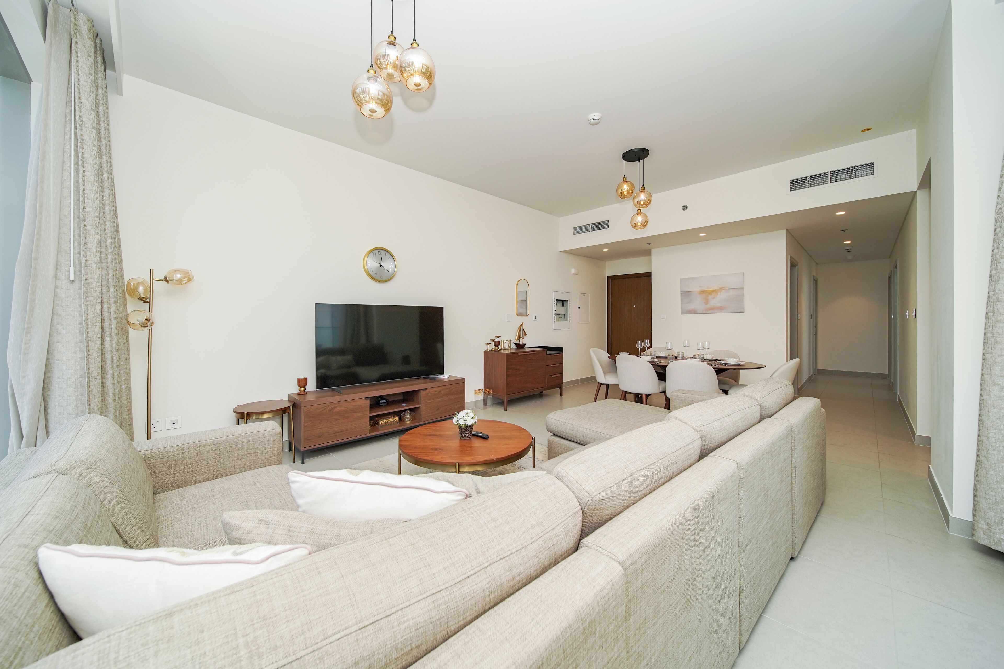 A modern living room with a large sofa, a TV, and a dining area with a table and chairs.