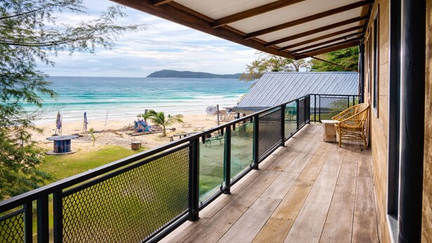A wooden deck with a glass balustrade overlooking a beach with a clear view of the ocean and distant land. - Seaside Cenang (Langkawi)
