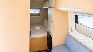 A compact RV interior with a bed, a small window, and a kitchenette area. - Seaside Cenang (Langkawi)