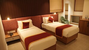 A hotel room with two beds, a nightstand, a green chair, and a wooden cabinet.