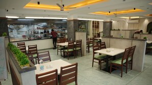 A restaurant with wooden tables and chairs, a kitchen area, and a person working behind the counter.