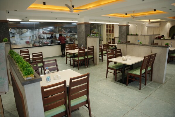 A restaurant with wooden tables and chairs, a kitchen area, and a person working behind the counter. - Denz Paradise (Iritty)