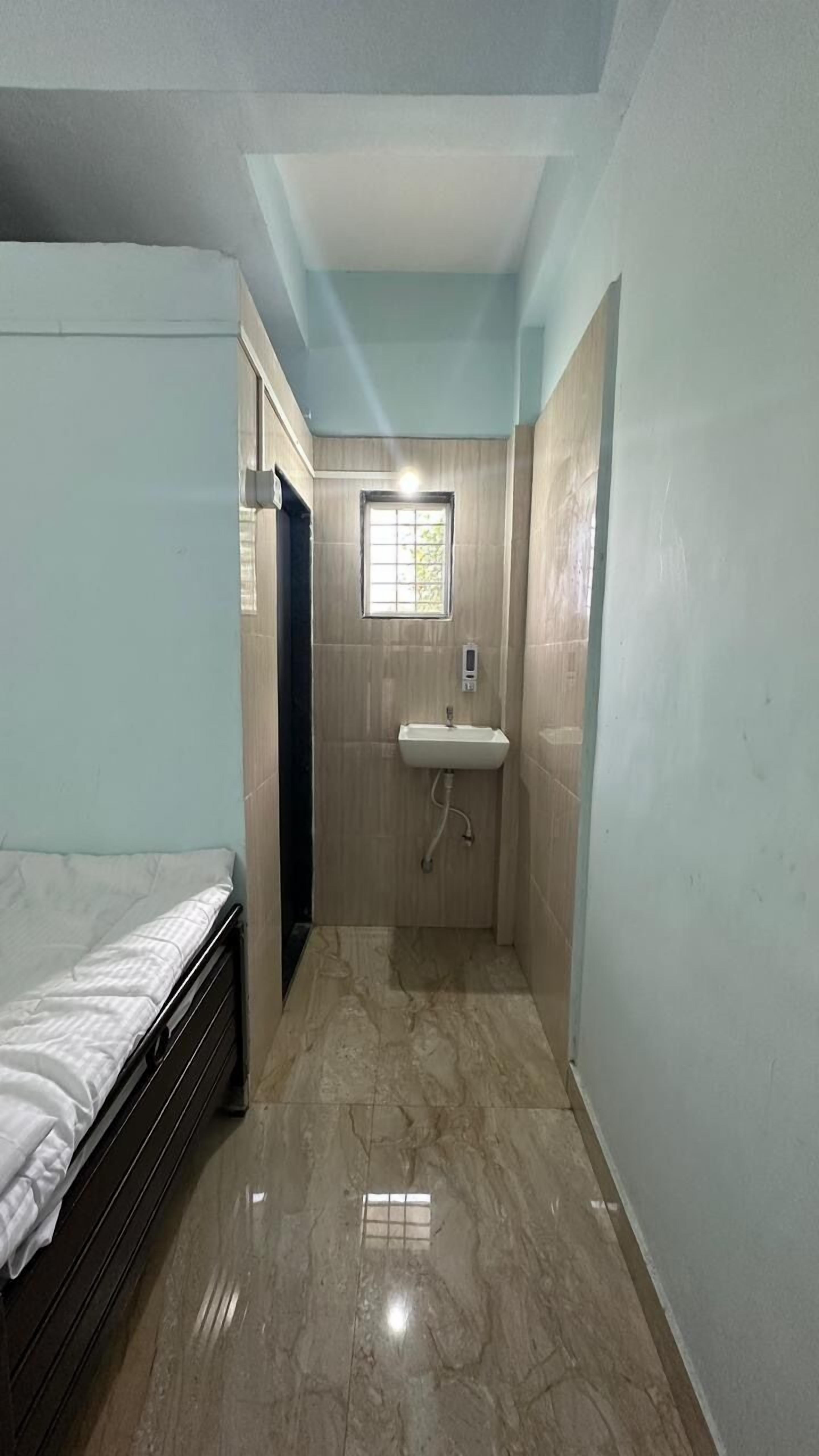 A small, narrow room with a bed on one side and a bathroom with a sink and window.