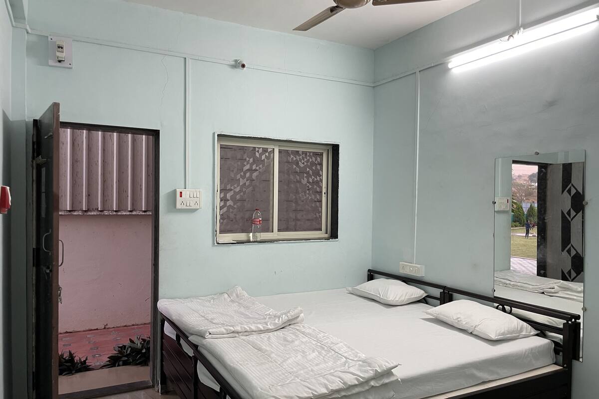 A bedroom with a single bed, a ceiling fan, a window with patterned blinds, and a door leading to an outdoor area.